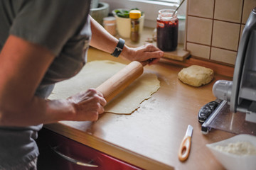 Selective focus shot of a female roll out the dough with a wooden rolling pin in the kitchen