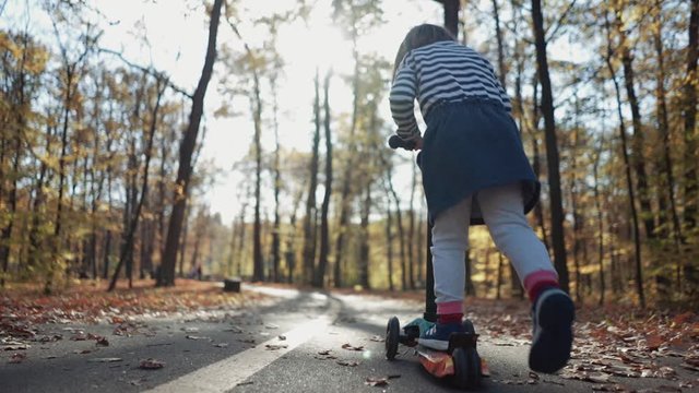 Little girl riding a scooter in autumn park, slow motion