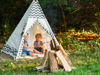 Two young boys playing in a backyard teepee campsite under the summer sunset