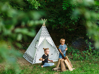 Two young kids roast marshmallows in the backyard next to a play teepee