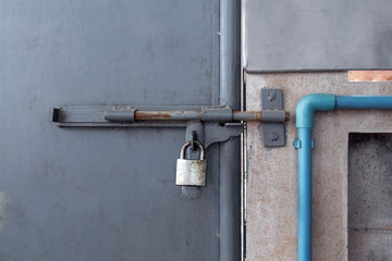 Old locked padlock on the gray gate of rusty metal steel of factory background.