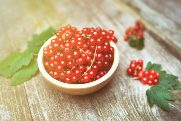 Fresh ripe red currant berries with leaves in a bowl on rustic old wooden table. Healthy organic food, summer vitamins, BIO viands, natural background. Copy space for your advertising text message