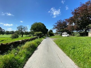 Country lane, with grass verges, dry stone walls, trees and fields, on a summers day in, Rylstone, Skipton, UK
