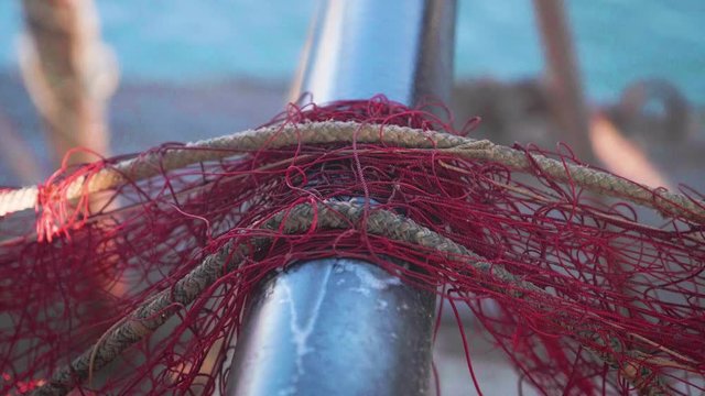 Fishing net close up, harbour workers at work. Fishermen arranging some red fishing nets at harbour. Exterior, daytime. Slow motion