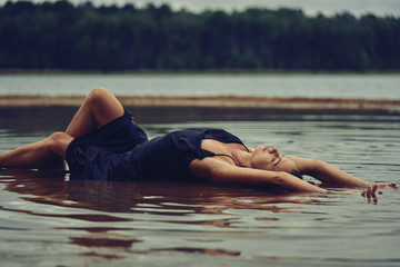 lying girl in a long black dress on the shore of the bay, the concept of the joy of health, sleep and relaxation             