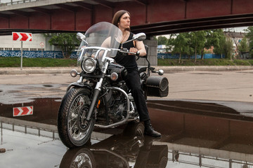 Long-haired guy on a black motorcycle under the bridge reflected in big puddle