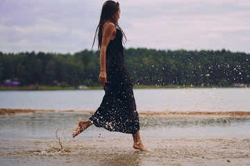girl in a long black dress runner on the water on the shore of the bay, the concept of the joy of...