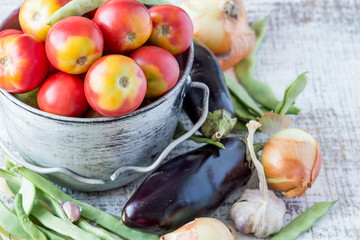 Fresh vegetables. Ripe red tomatoes in an old aluminum bucket, next to eggplant, onion, garlic and green bean pods. Selective focus.