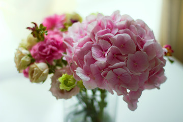 Bouquet of pink flowers in  glass vase on  white table. Spring or summer greeting card with flowers. Mother's Day Greeting Card. Happy Birthday or Valentine. Women's Day. Copy space.