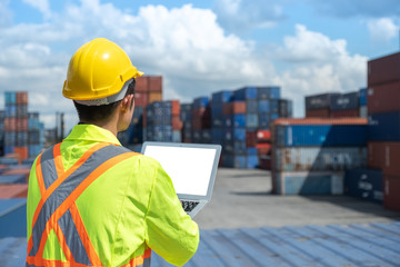 backview shipping worker or engineer using blank screen laptop in shipyard factory with containers and sky background with screen clipping path