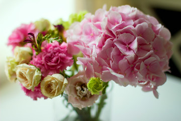 Bouquet of pink flowers in  glass vase on  white table. Spring or summer greeting card with flowers. Mother's Day Greeting Card. Happy Birthday or Valentine. Women's Day. Copy space.