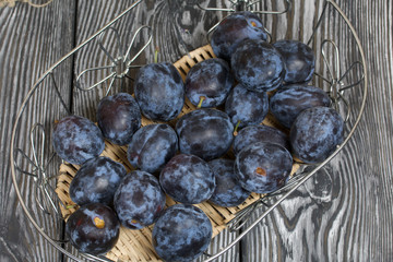 Ripe plums in a basket. On painted pine planks. Filmed from above.