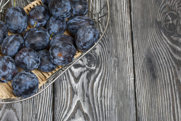 Ripe plums in a basket. On painted pine planks. Filmed from above.