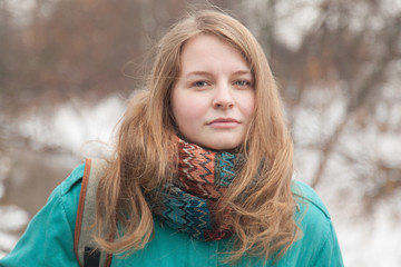 Girl with long blond hair in a turquoise jacket with a bright scarf in a winter park