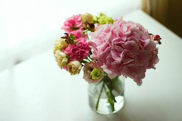 Bouquet of pink flowers in  glass vase on  white table. Spring or summer greeting card with flowers. Mother's Day Greeting Card. Happy Birthday or Valentine. Women's Day. Copy space.