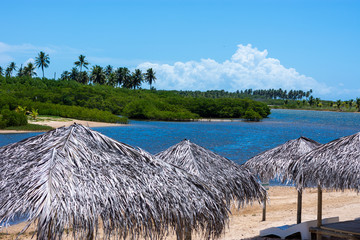 V&aacute;rios quiosques na praia com uma ilha ao fundo
