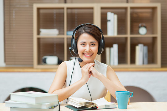 Happy Asian Chinese business woman with headphones looking at camera learning online course or job interview working at home