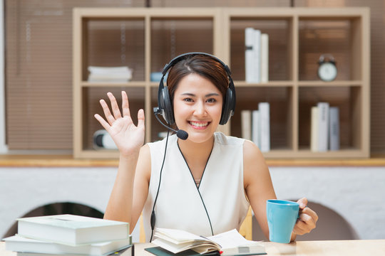 Happy Asian Chinese business woman with headphones looking at camera learning online course or job interview working at home