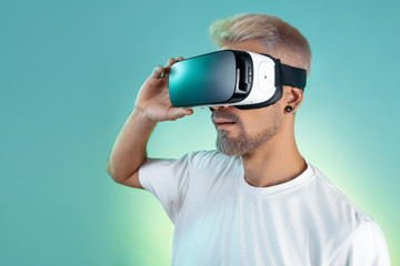 Suprised bearded hipster man with blonde hair wearing virtual reality goggles in studio in neon lights.