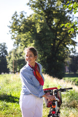 Happy young woman walking bike in park