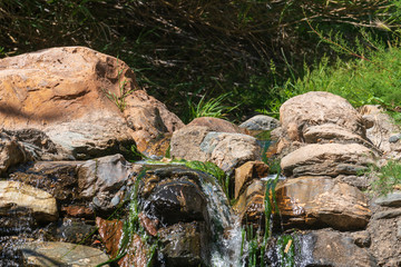 water flowing between the stones, there is vegetation and a stone wall


