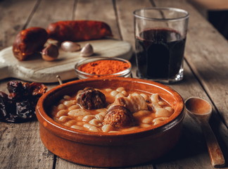 Asturian bean stew on wooden table together with some ingredients and a glass of wine