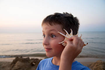 handsome boy with a surprised expression on his face listens to a seashell. The concept of cheerful and joyful emotions.