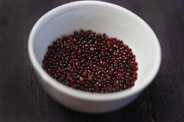 Dark red beads in a white cup on a black background