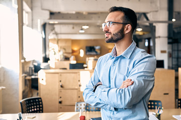 Business Concept. Man in shirt and eyeglasses standing close-up on office background crossed hands...