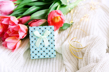 Gift box and bouquet of pink tulips on bed