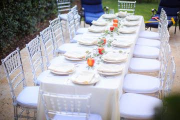 Formal Thanksgiving table in the fall family group get together tradition using white plates in beautiful outdoor setting red apples and green leaves centerpiece.