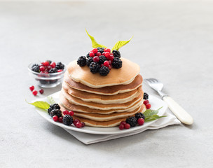 Pancakes with fresh berries on a plate on a light background