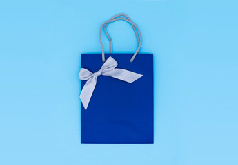 A blue gift bag with a silver ribbon on blue background. Top view, copy space. Gift concept. New year, Woman's day. Valentine's day. Ready for birthday party.