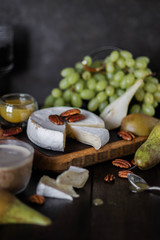Fototapeta na wymiar Camembert cheese on a wooden board among fruits, nuts and drinks. Snack table setting. Gourmet food.