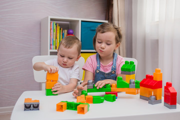 a little boy and a girl are playing a game of constructor at a table in a room
