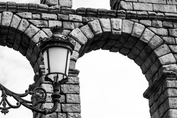Low angle grayscale shot of a street lamp near an old stone bridge