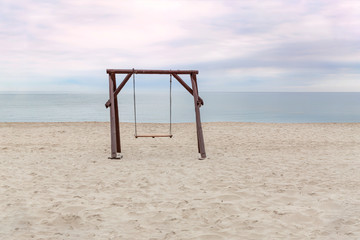 A large wooden swing on an empty beach against the background of the sea and sky
