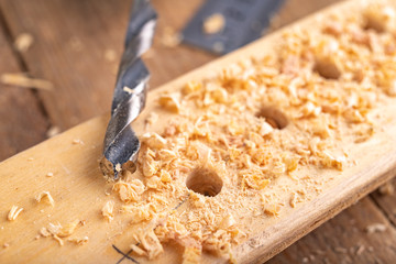 Creating holes with a metal drill in a piece of wood. Minor carpentry work in a home workshop.