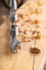 Creating holes with a metal drill in a piece of wood. Minor carpentry work in a home workshop.
