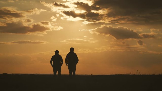 Two friend tourists walk along the lake at sunset. Traveling with backpacks in warm weather in summer. Healthy lifestyle concept.
