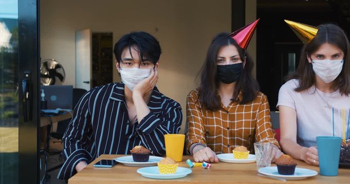 Sad birthday party with COVID-19 safety measures. Slide along young upset multiethnic friends in face masks slow motion.