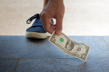 Male hand picking up one dollar bill from the ground.