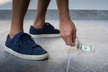 Anonymous man, casual dressed, with blue sneakers, picking up one dollar bill from the floor.