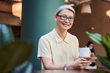 Fototapeta na wymiar Cheerful woman smiling happily while enjoying hot beverage in cafe