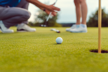 Pro on golf course teaching a woman how to put - 373166805