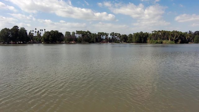 stunning aerial shot flying over the lush green waters of Lake Evans at Fairmount Park with blue skies and clouds and lush green trees and plants