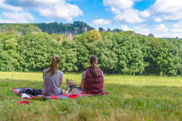 2 junge Frauen machen mit Ihrem Hund ein Picknick in der säschsichen Schweiz bei Rathen auf einer Decke vor wunderschöner Landschafts Kulisse