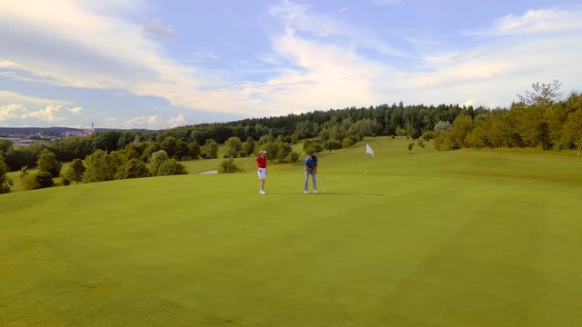 Woman and pro practicing putting on golf green, drone shot