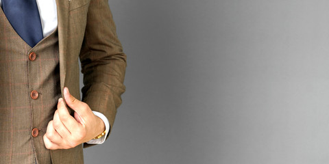 Portrait of a businessman in a suit, holding his hand over the edge of his jacket. No face visible. Gray background.