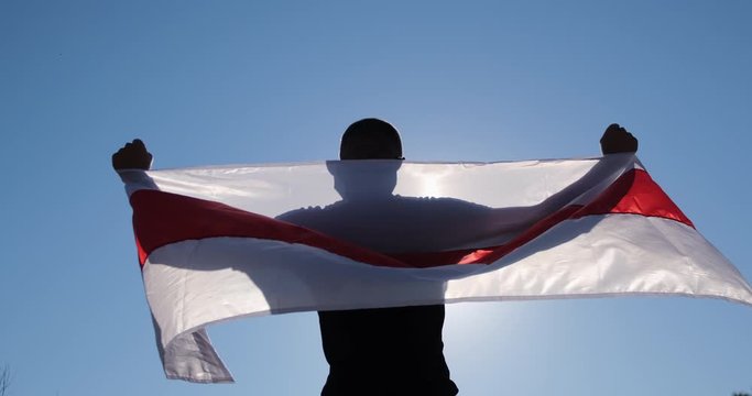 A man spreads the flag of Belarus with his hands on his back. The flag flutters in the wind.